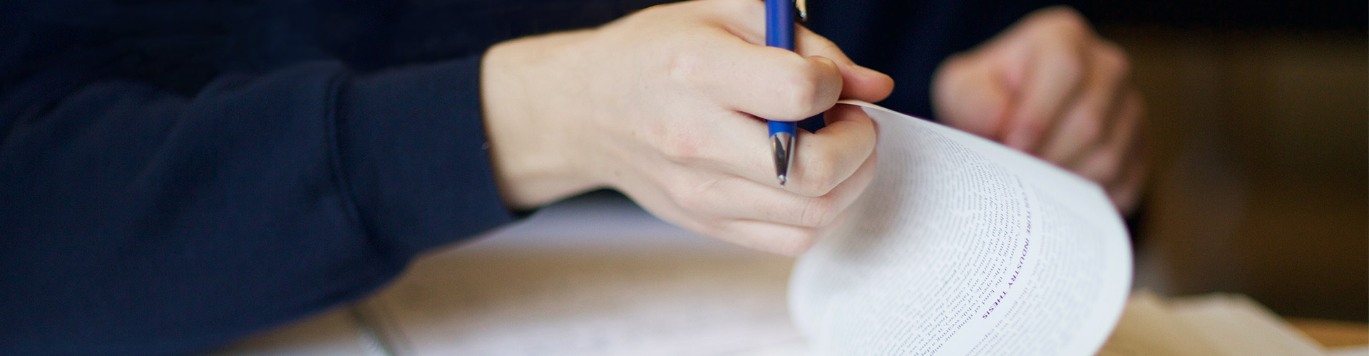 Person holding a pen and reading a book.