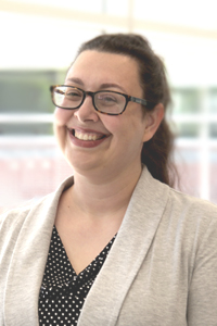 Photo of Laura Mabee — Woman with dark hair in ponytail, wearing a grey blazer. 