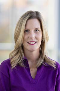 Photo of Jackie Denison — women with shoulder-length, curly hair wearing a purple blouse. 